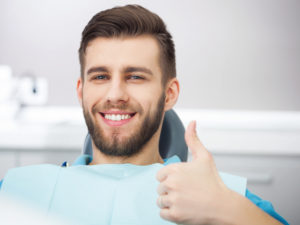 A young man in a dentist's chair giving a thumb's up.
