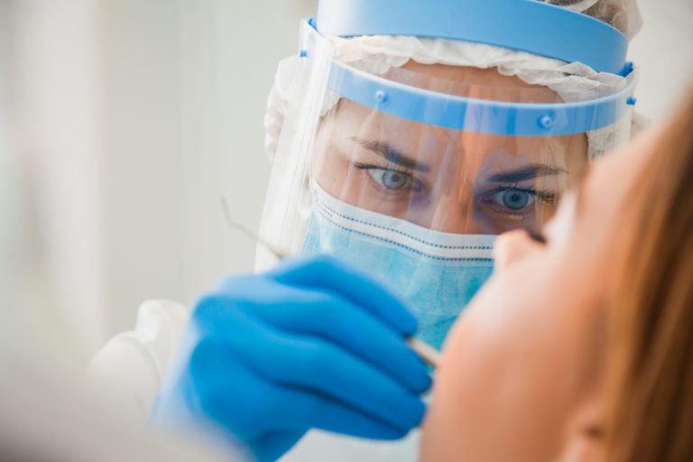 A dentist with a face guard examing a patient.