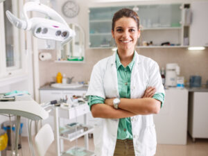 A dental professional standing in an exam room, smiling with their arms crossed.