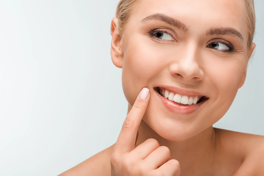 A young woman smiling while pointing to her teeth.
