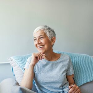A mature woman sitting in her living room, healthy and happy from holistic dentistry.