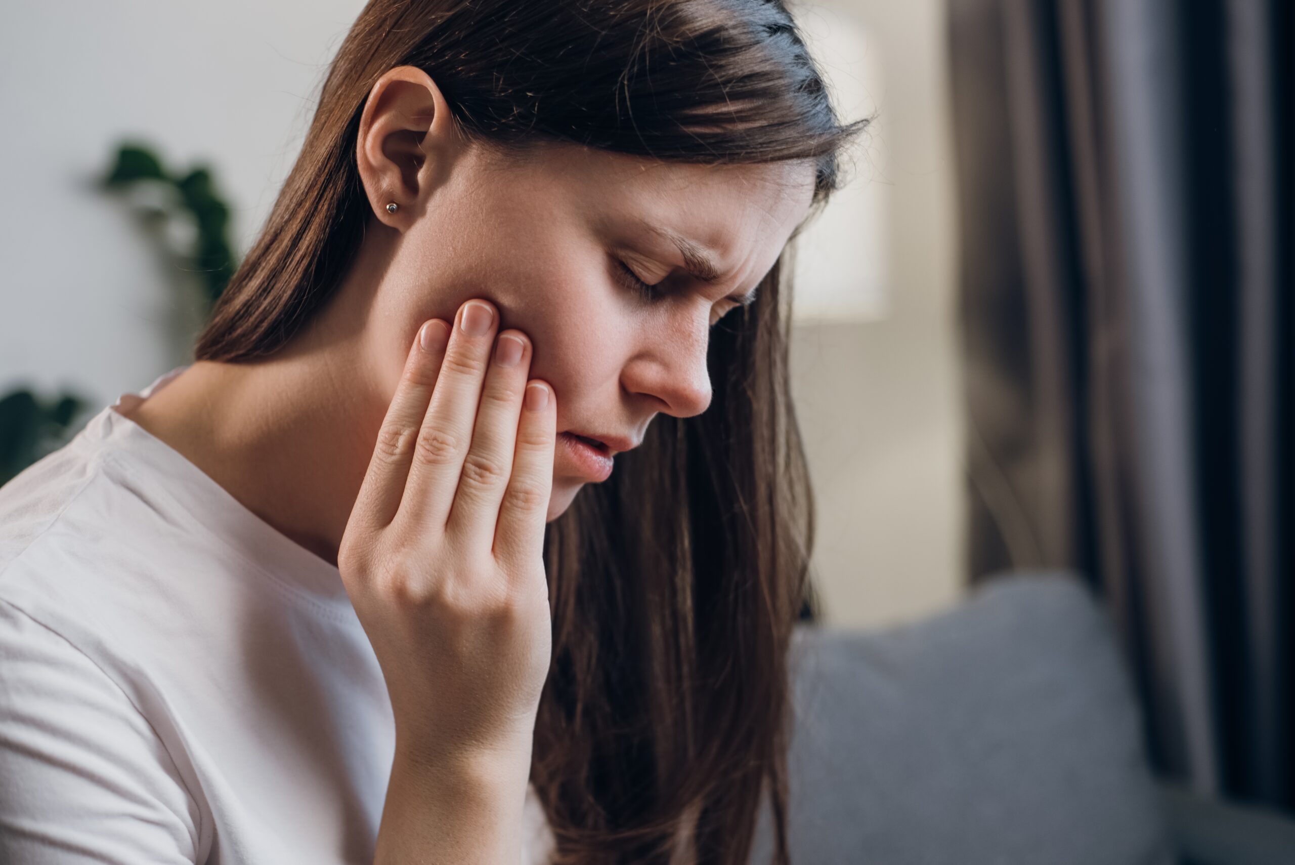 closeup of a woman suffering from jaw pain, hand on side of face