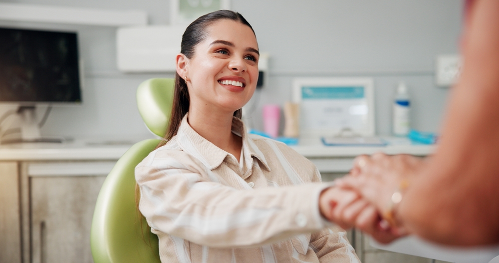 Woman,,Holding,Hands,And,Smile,At,Dentist,For,Oral,Hygiene, young woman smiling, shaking hands with dental assitant