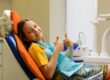 A cheerful schoolgirl gives a thumbs-up while sitting in a dental chair after a routine dentist appointment