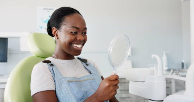 Happy,,Black,Woman,And,Dental,Teeth,With,Mirror,For,Clean smiling woman in a dental chair looking in mirror, perfect white teeth